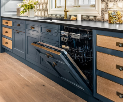 A kitchen with blue and wood panel cabinets. There's an opened JennAir dishwasher with the top and middle racks pulled out. On the counter are a glass container filled with various items, a potted plant and a toaster.